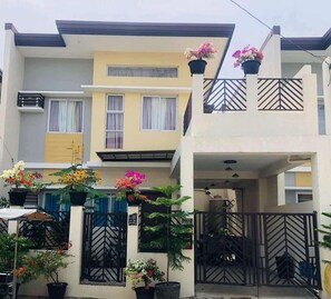 A two-story residential building with balconies, potted plants, and a gated entrance.