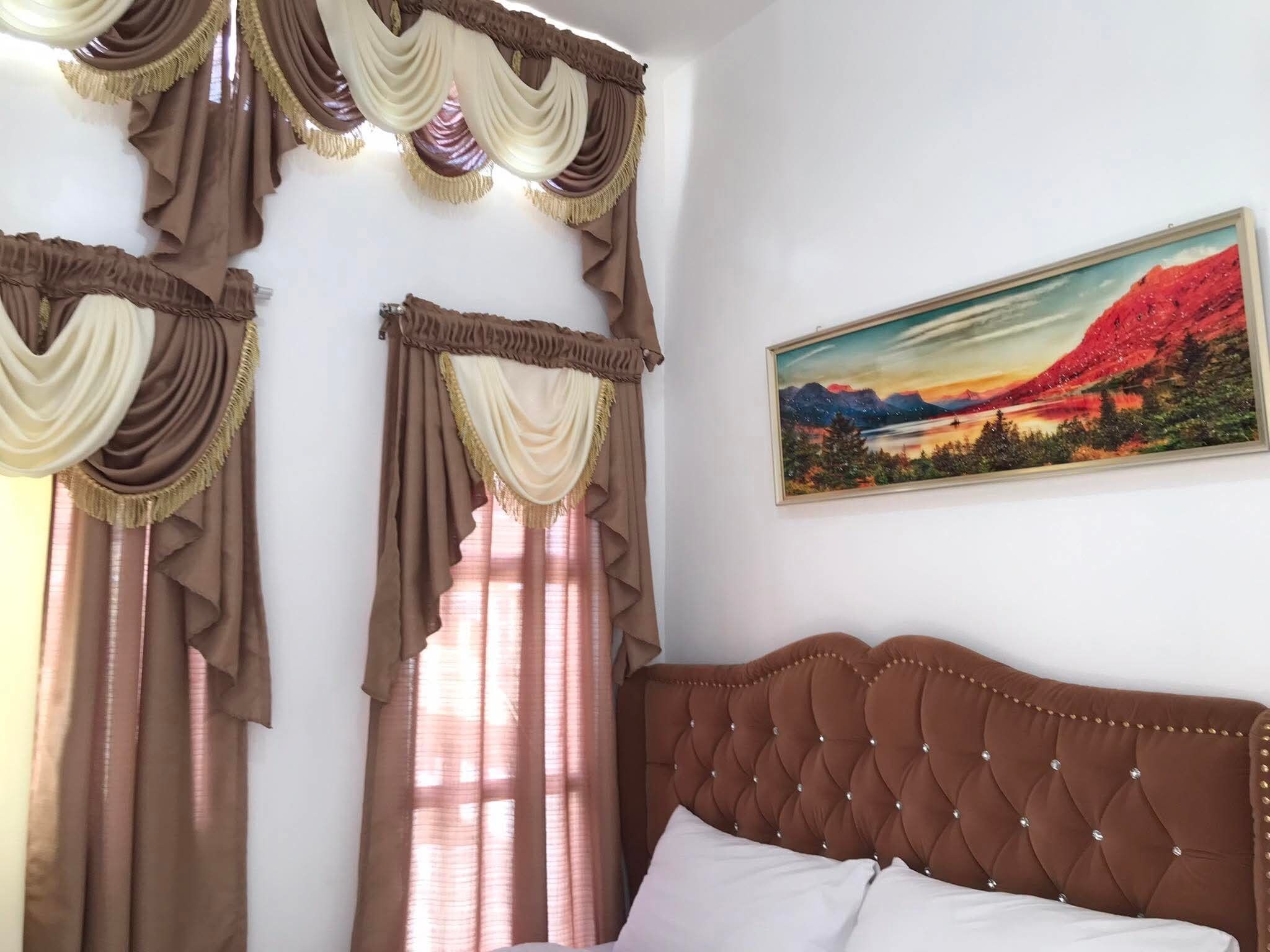 A bedroom with a large bed, curtains, and a painting on the wall.