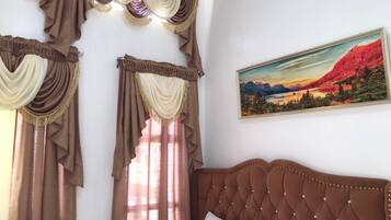 A bedroom with a large bed, curtains, and a painting on the wall.