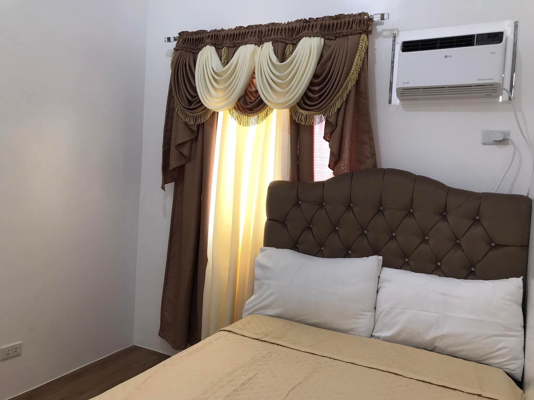 Ein Schlafzimmer mit einem Bett, Vorhängen, einer Klimaanlage und einer Steckdose.