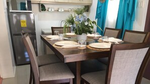 A dining table set with plates, glasses, and a vase of flowers, surrounded by chairs. - Superhost Home - 2 min Airport -Pool WiFi - Samal (Davao)