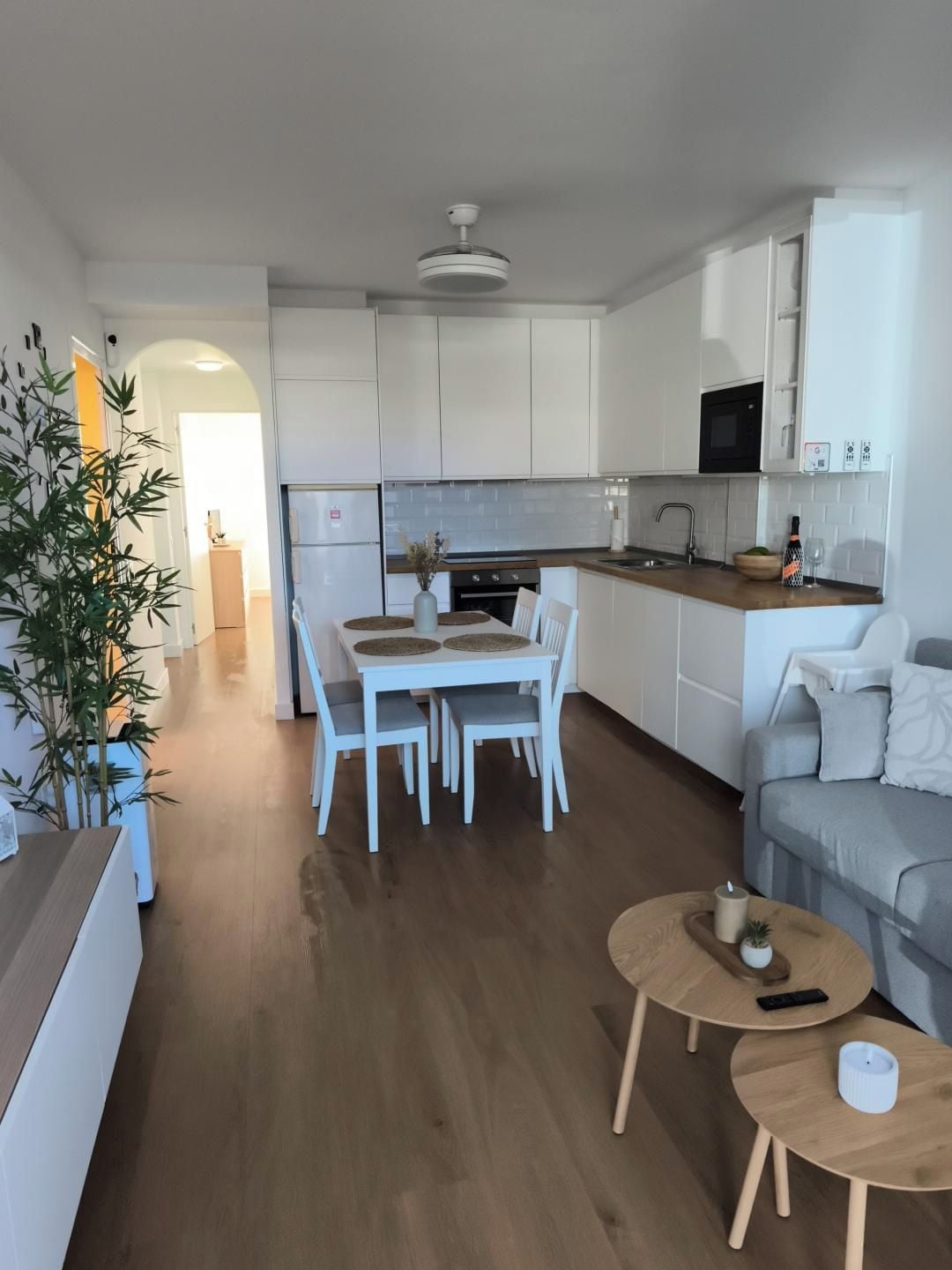 A modern kitchen with white cabinets, a dining table with chairs, a sofa, and two small wooden tables with candles.