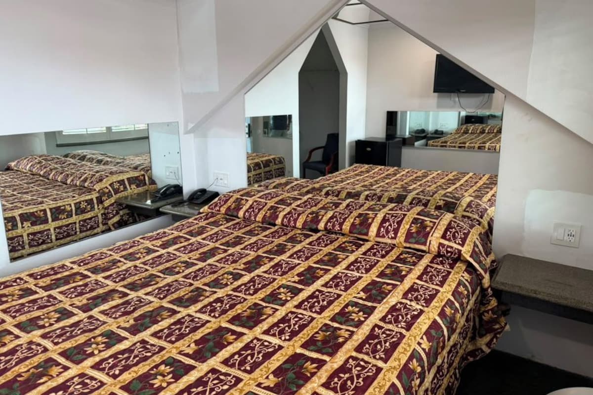 A bedroom with a mirrored ceiling, a bed with a patterned bedspread, a desk, and a chair.