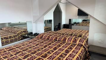 A bedroom with a mirrored ceiling, a bed with a patterned bedspread, a desk, and a chair.