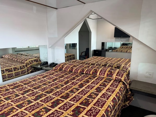 A bedroom with a mirrored ceiling, a bed with a patterned bedspread, a desk, and a chair.