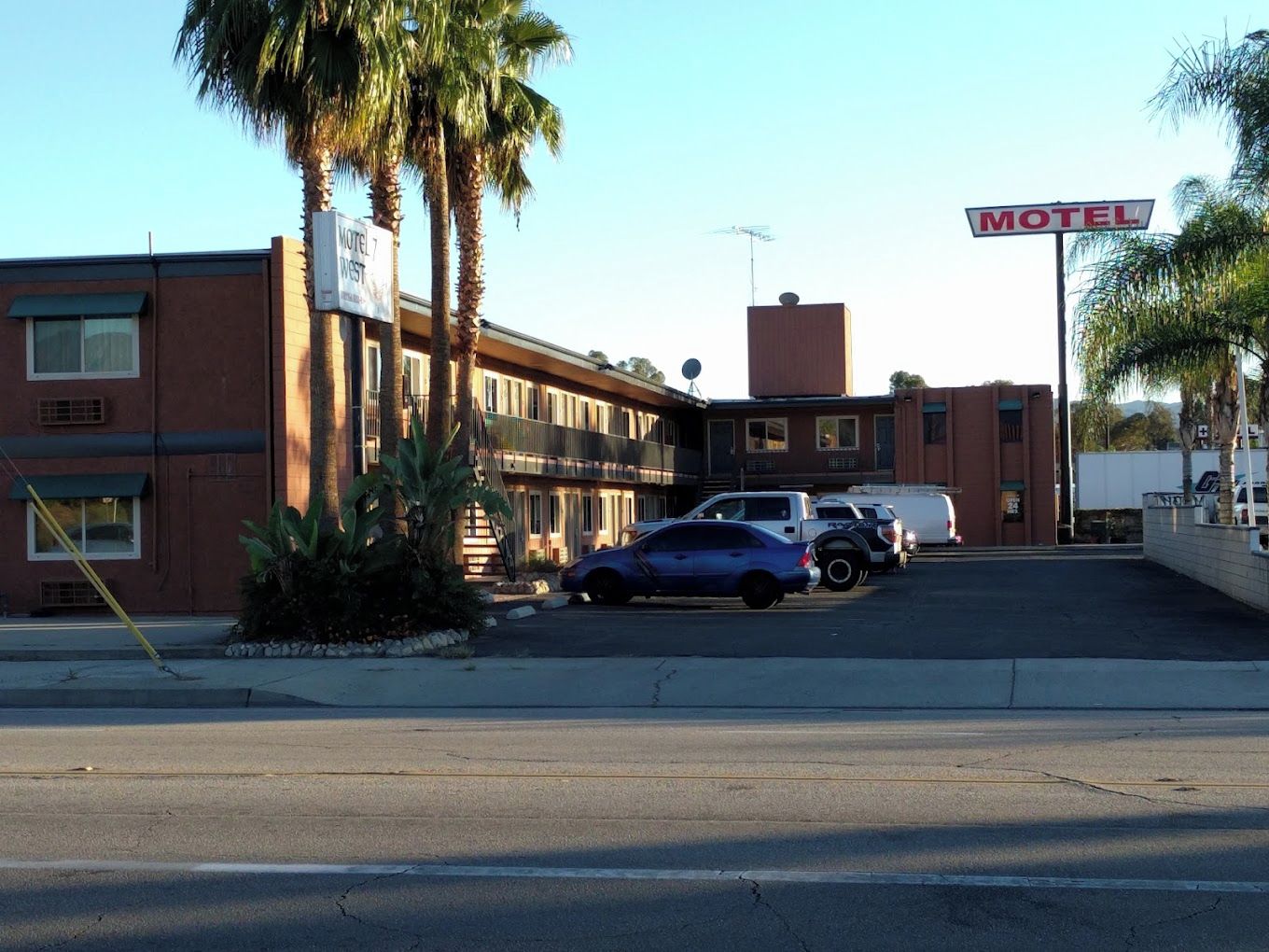 A motel with a sign, parked cars, and palm trees.