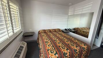 A hotel room with a bed, a mirror, a heater, and a window with blinds.