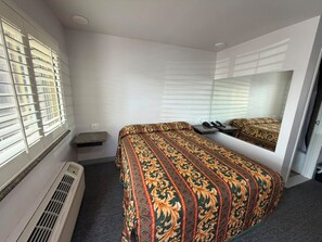 A hotel room with a bed, a mirror, a heater, and a window with blinds.