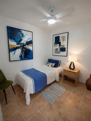 Un dormitorio con cama, mesita de noche, lámpara, silla y dos cuadros abstractos en la pared.