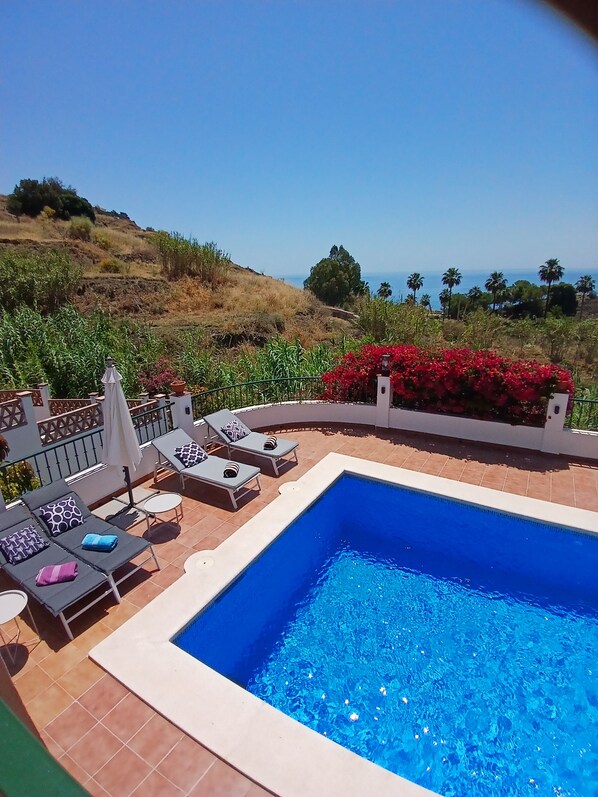 Una piscina con sillones de descanso y vistas al mar.