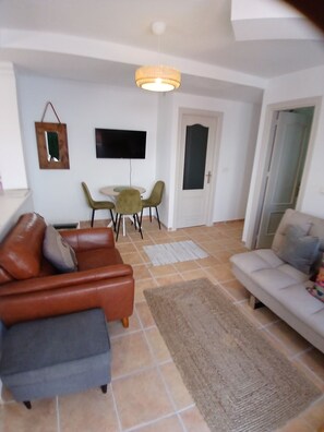 A living room with a brown leather sofa, a grey sofa, a TV mounted on the wall, and a dining area with a table and chairs. - Cosy private two bed apartment with exclusive use of swimming pool. (Torrox)