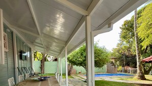 A covered patio area with a dining table set for six, outdoor pool, and a stone-tiled floor. - Country house with sand court and heated pool. (Americana)