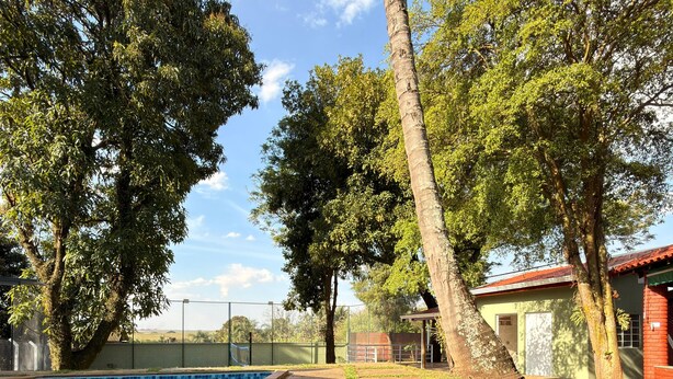 A swimming pool with a tiled edge, surrounded by a stone patio and trees. - Country house with sand court and heated pool. (Americana)