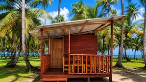 A wooden structure with a porch, a door, and a view of the beach and palm trees. - cabaña madera sanblas luxury  (Nusatupo)