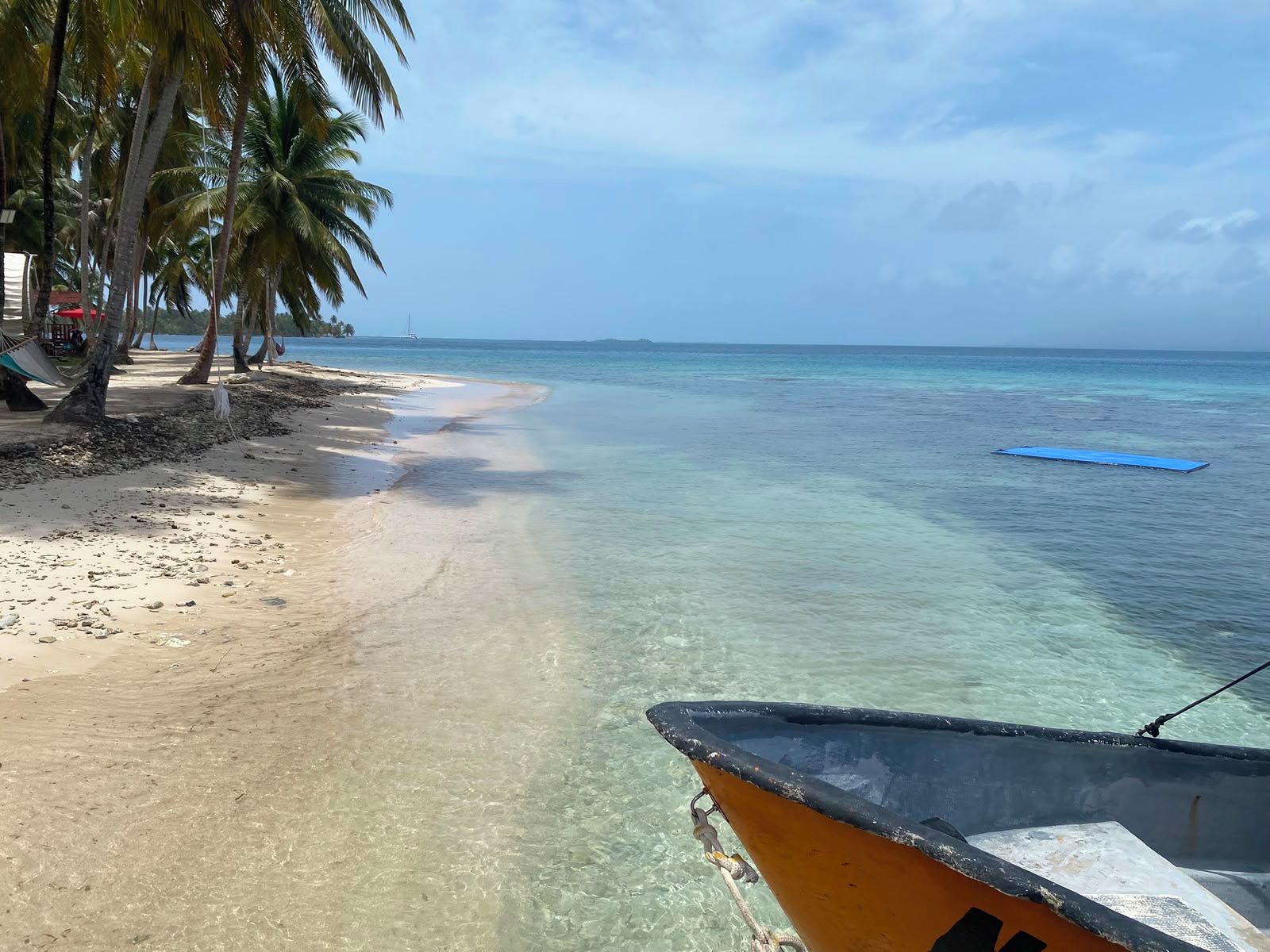 Una playa con agua cristalina, orilla de arena y un bote.
