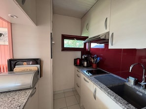 Eine kompakte Küche mit Einbauofen, Spüle und einem Fenster mit Blick auf Grünflächen.