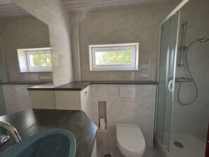 Ein modernes Badezimmer mit Dusche, Toilette und Waschbecken. Zwei Fenster sorgen für natürliches Licht.