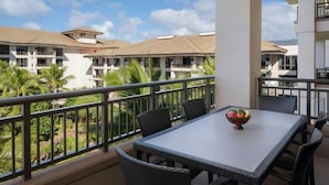 Un balcon agrémenté d’une table et de chaises, donnant sur un jardin luxuriant et sur un immeuble doté de nombreux balcons.
