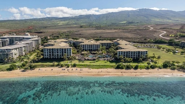 Un complexe hôtelier comprenant plusieurs bâtiments, une plage et un paysage montagneux en arrière-plan.