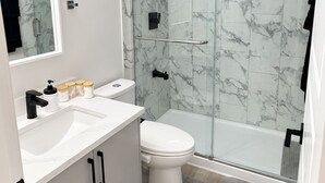 Ein modernes Badezimmer mit einer Duschkabine, einer weißen Toilette und einem Waschtisch mit Spiegel und Waschbecken.
