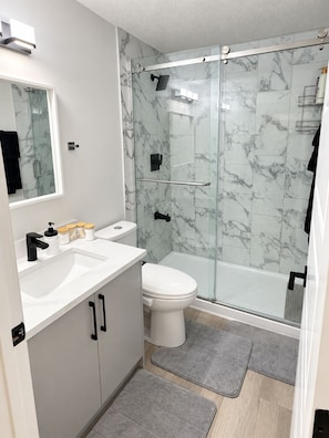 Et stilfuldt badeværelse med et glasvægshus, et hvidt toilet og en vaskepult med spejl og håndvask.