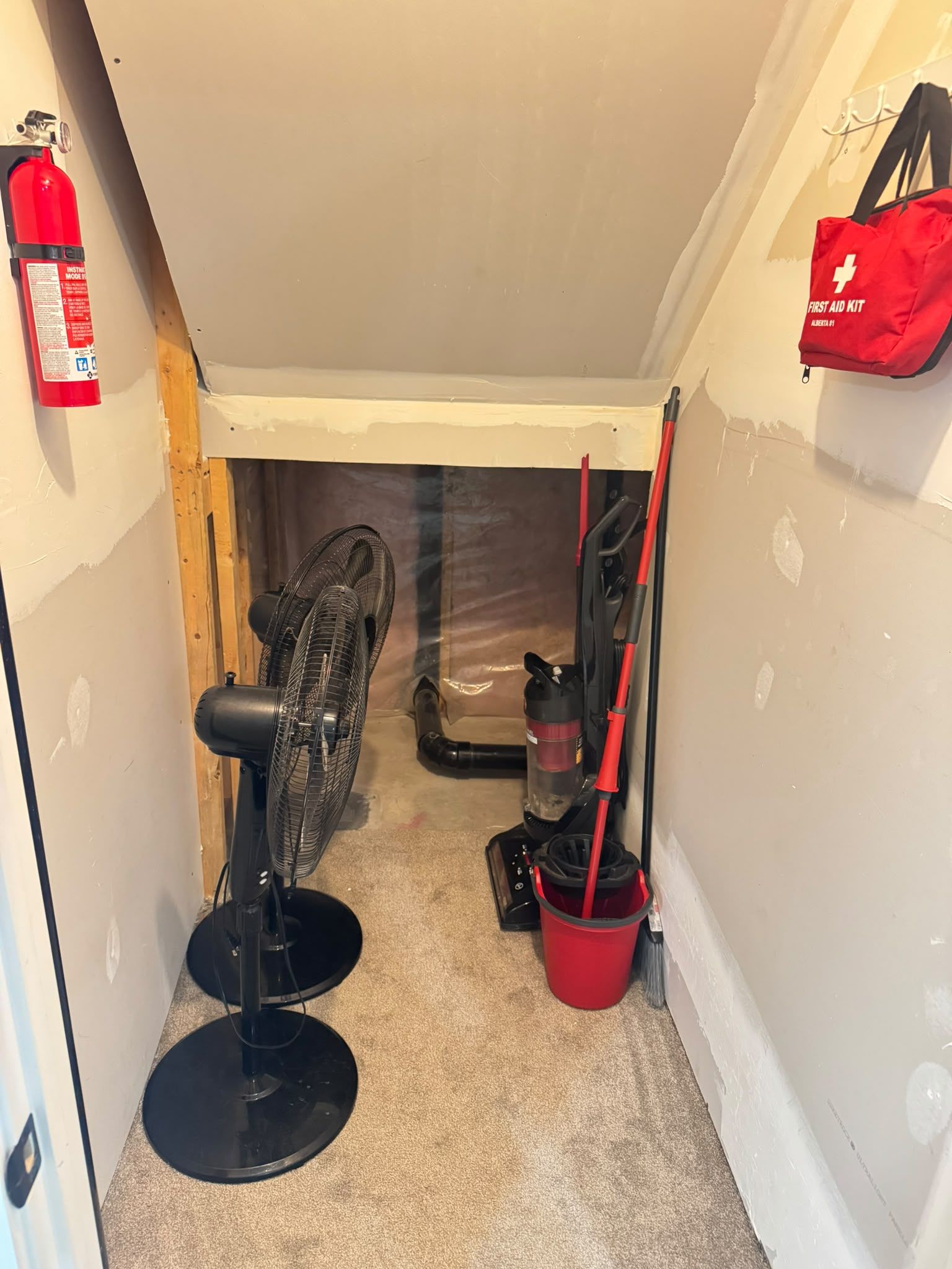 A narrow hallway with a fire extinguisher, a first aid kit, a fan, and a mop bucket.