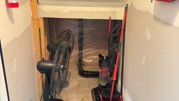 A narrow hallway with a fire extinguisher, a first aid kit, a fan, and a mop bucket.