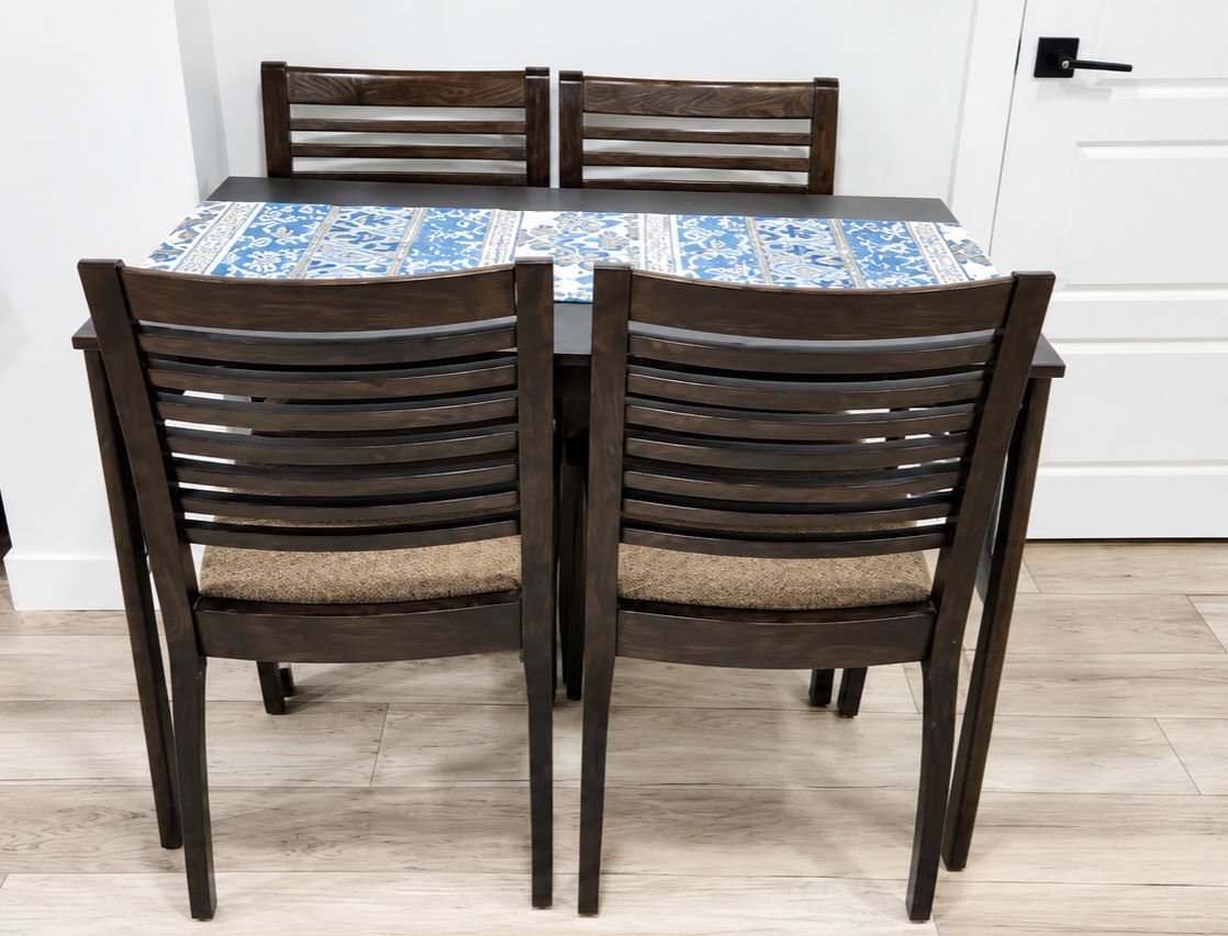 Ett matbord med ett mönstrat bordsduk, omgivet av fyra mörka trästolar med vadderade sitsar.