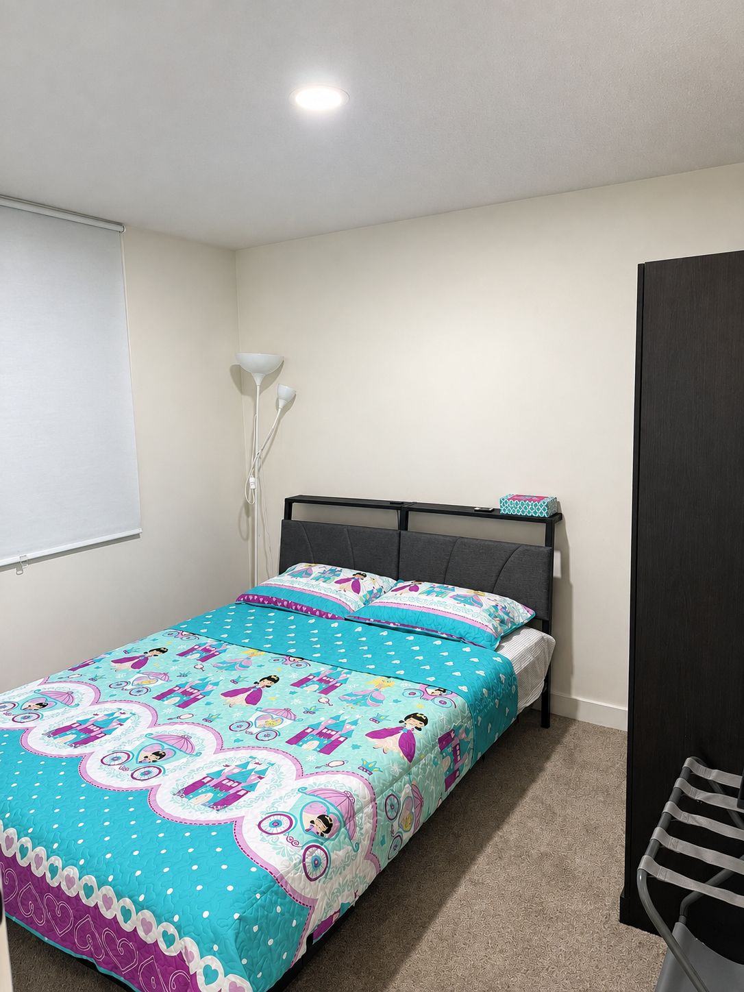 A bedroom with a bed, a bedside table, a lamp, and a wardrobe.