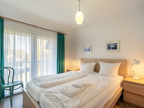 Ein Hotelzimmer mit einem Bett, zwei Nachttischen, einem Sessel, einem Fenster mit Vorhängen und zwei gerahmten Bildern an der Wand.
