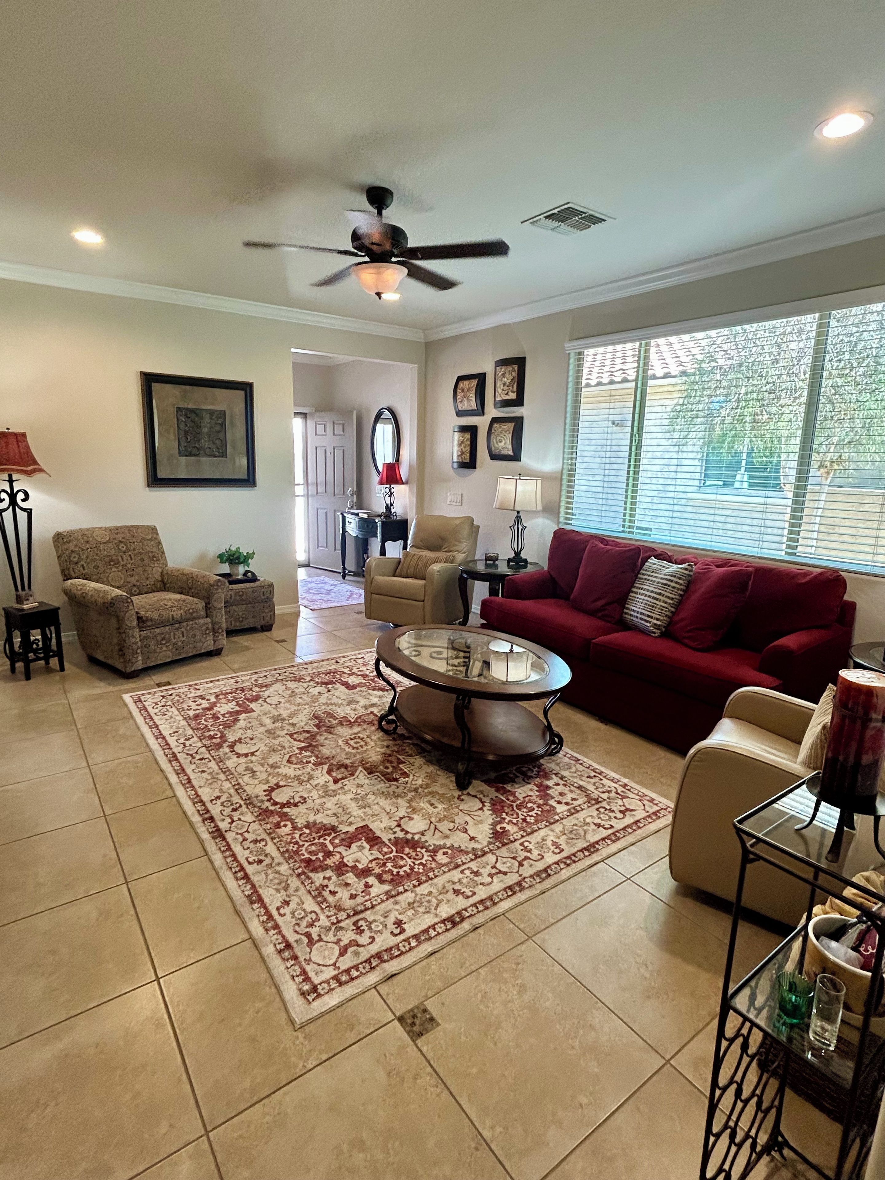 A living room with a red sofa, patterned armchairs, a coffee table, and a ceiling fan.