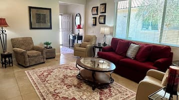 A living room with a red sofa, patterned armchairs, a coffee table, and a ceiling fan.