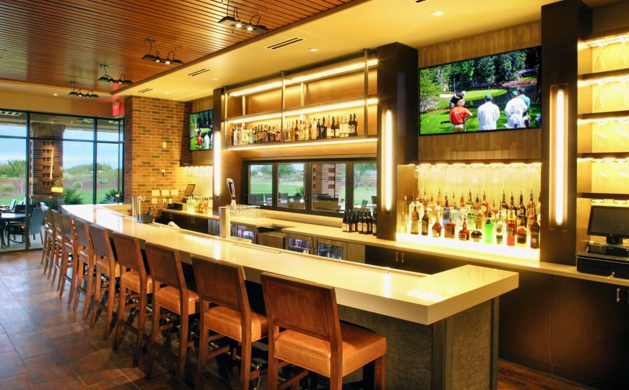 A bar area with a long counter, multiple seating options, and a television screen displaying a golf game.