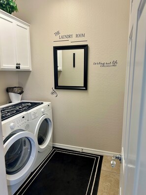 A laundry room with a washing machine, a dryer, and a mirror on the wall. - Desert Oasis in 55+ Merrill Ranch (Florence)