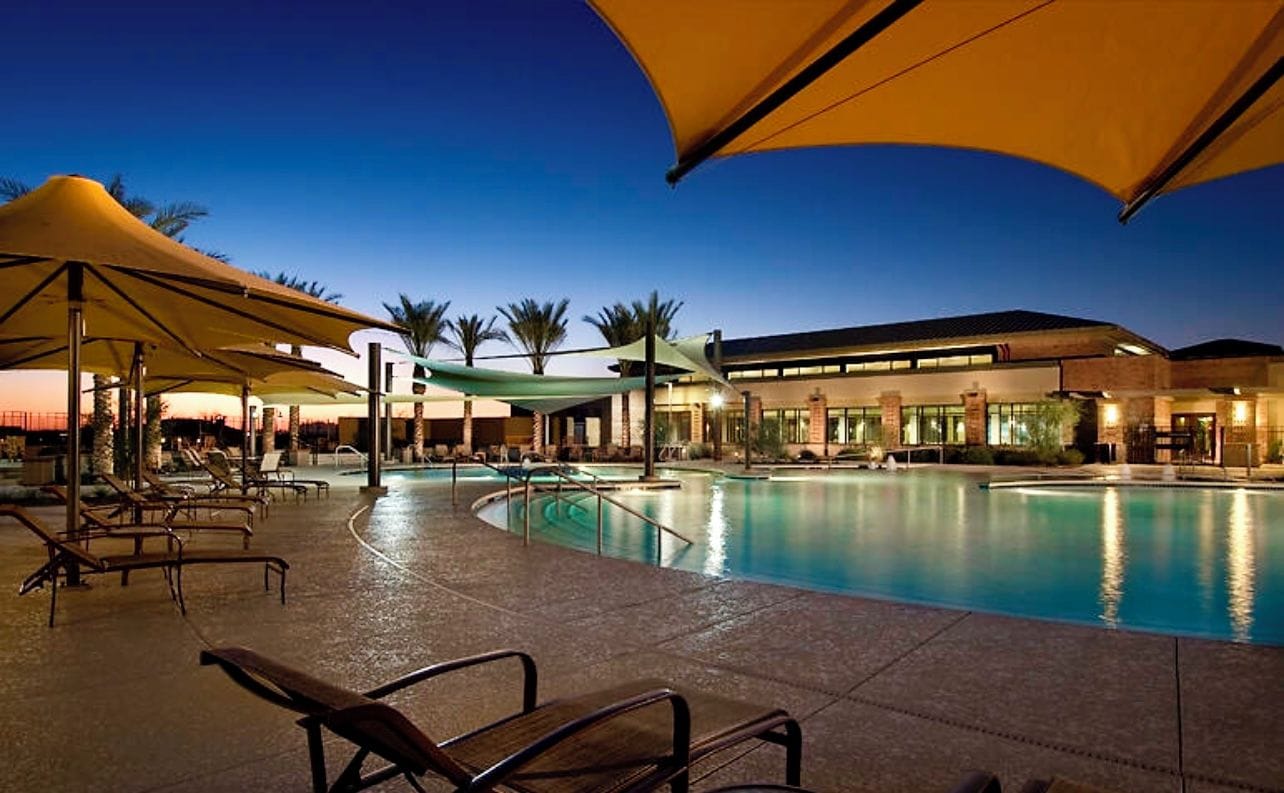 A swimming pool area with lounge chairs and umbrellas, surrounded by a building with a modern design.
