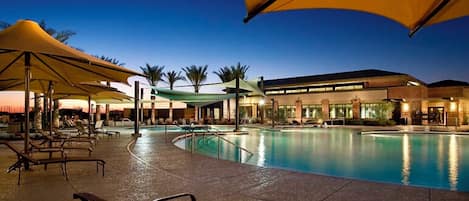 A swimming pool area with lounge chairs and umbrellas, surrounded by a building with a modern design.