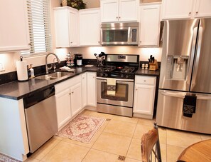 A modern kitchen with white cabinets, stainless steel appliances, a black countertop, and a patterned rug. - Desert Oasis in 55+ Merrill Ranch (Florence)
