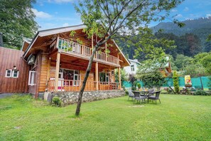 A wooden cabin with a balcony, surrounded by a grassy yard and trees. - DanCenter Riverside Lexus Regency (Pahalgam)
