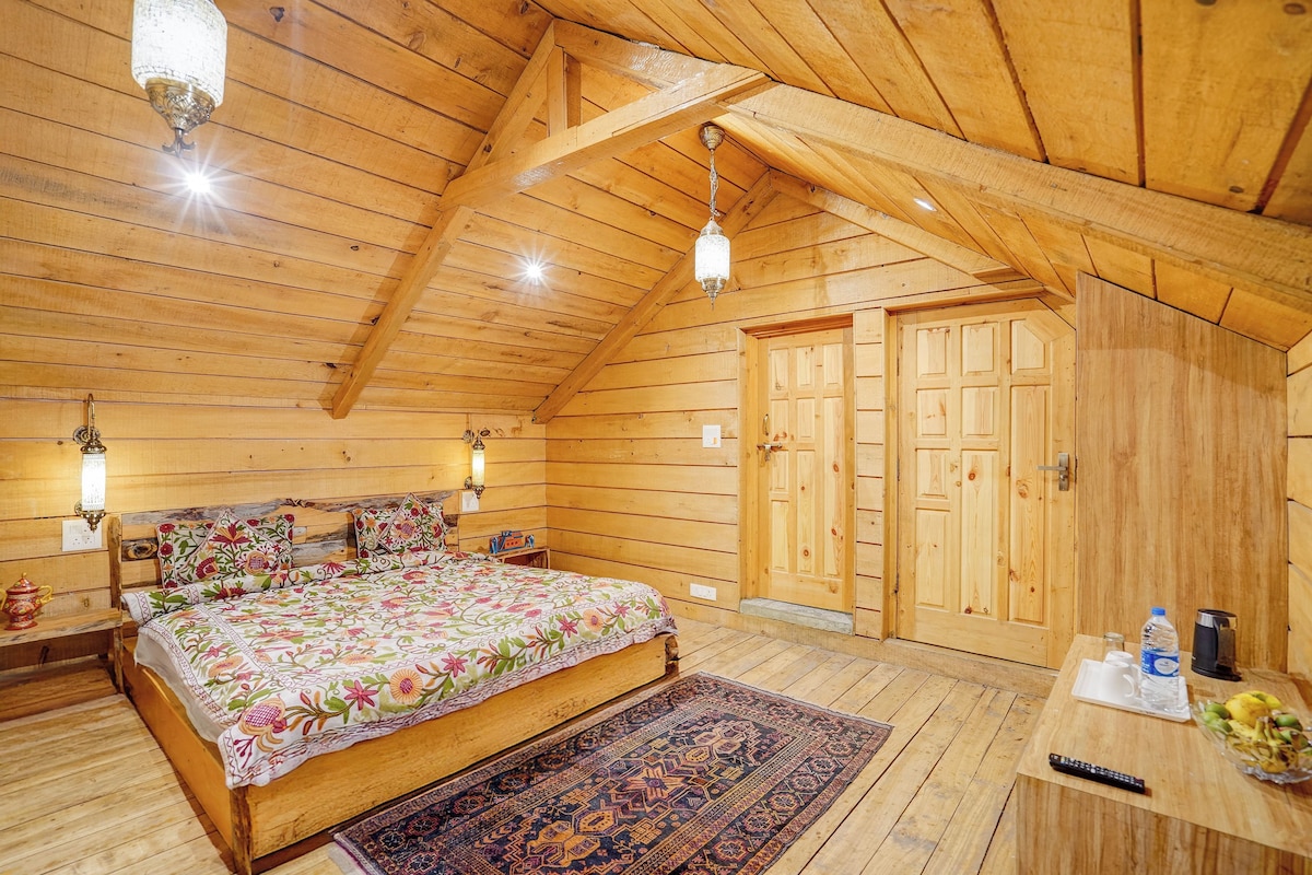 A wooden interior with a bed, a nightstand, a rug, and a door.