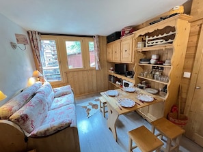 A cozy room with a sofa, a dining table set for two, wooden cabinets, and a window with curtains. - Cozy apartment, pets welcome - 4 guests (Avoriaz)