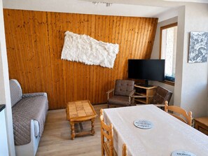 Ein Zimmer mit einer Holzwand, einem weißen Fellteppich, einem braunen Sofa, einem Holztisch mit Namensschild und einem Fernseher.