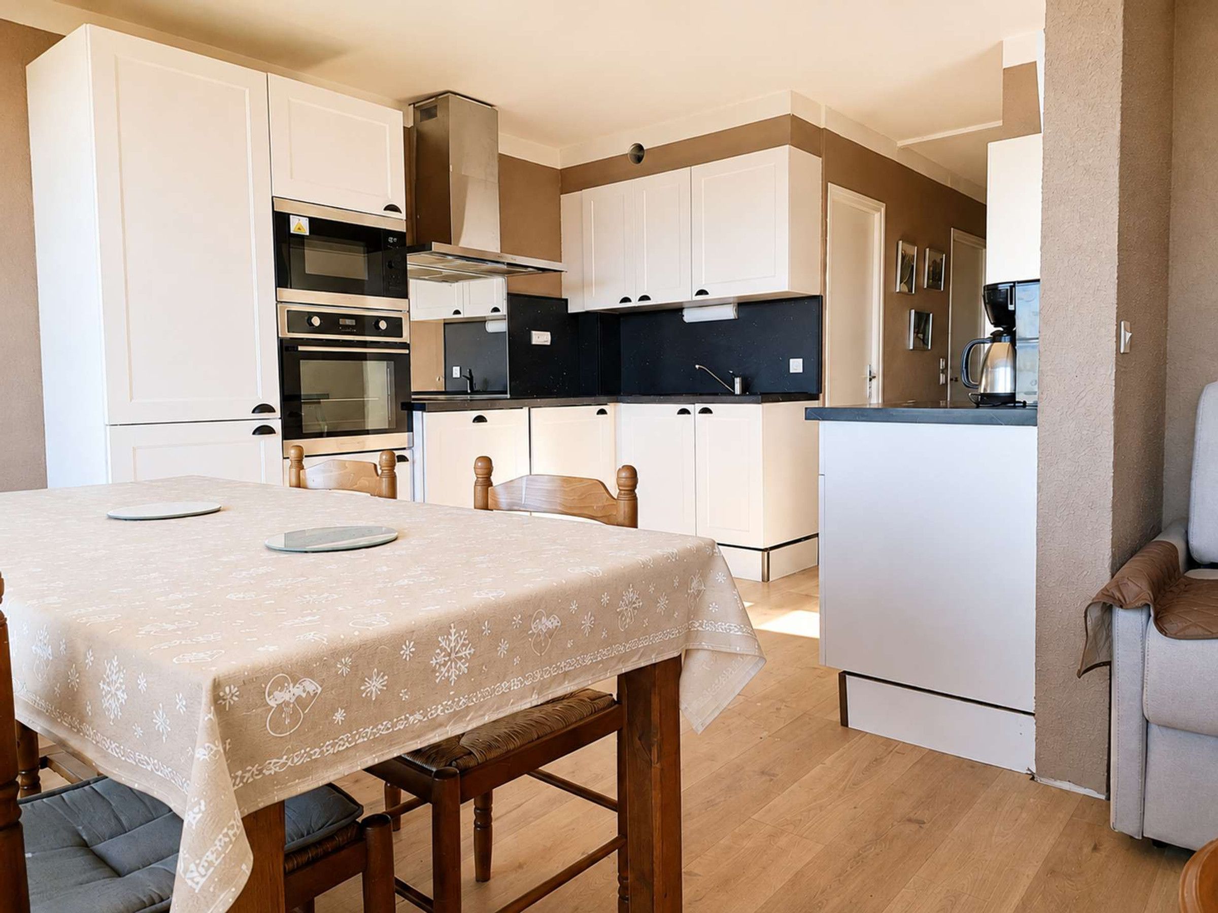 A compact kitchen with white cabinetry, a dining table with a festive tablecloth, and a small seating area with a bench.