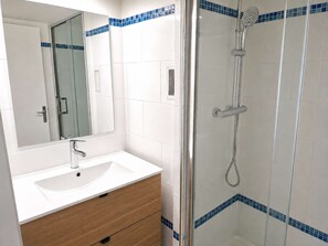 Ein Badezimmer mit einem weißen Waschbecken, einer Holzausstattung, einem Spiegel und einer Dusche mit Glaswand.