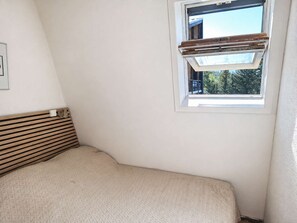 Una habitació amb un llit, una finestra amb persianes de fusta i un radiador.