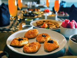 Une table dressée pour le petit-déjeuner, avec des viennoiseries sur une assiette, un bol de fruits et un verre de jus d’orange.