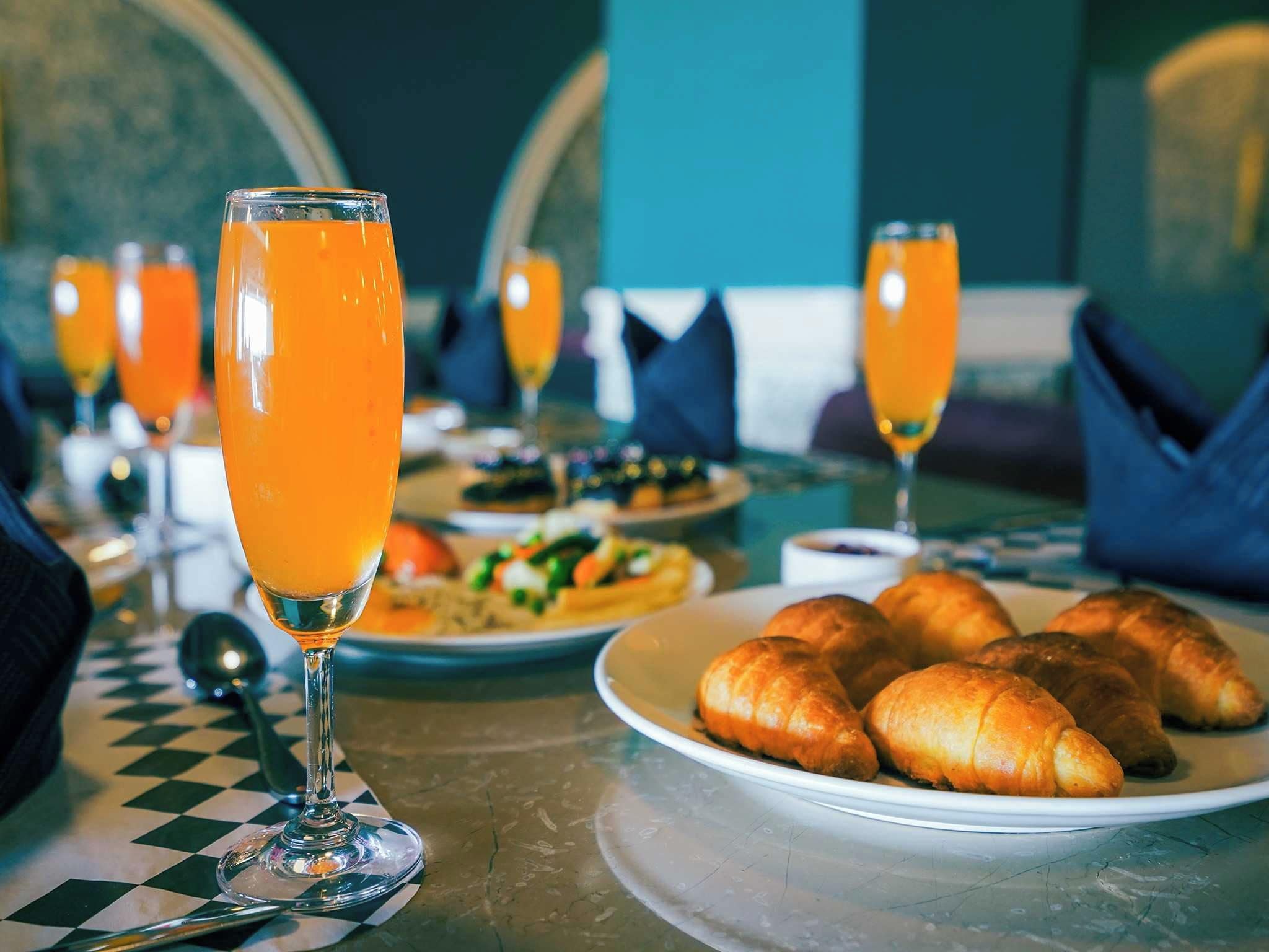 Ein Frühstückstisch mit Croissants, Orangensaft und einer karierten Tischdecke.