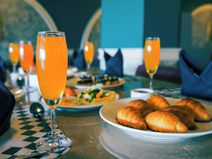 Une table dressée pour le petit-déjeuner avec des croissants, du jus d’orange et une nappe à carreaux.