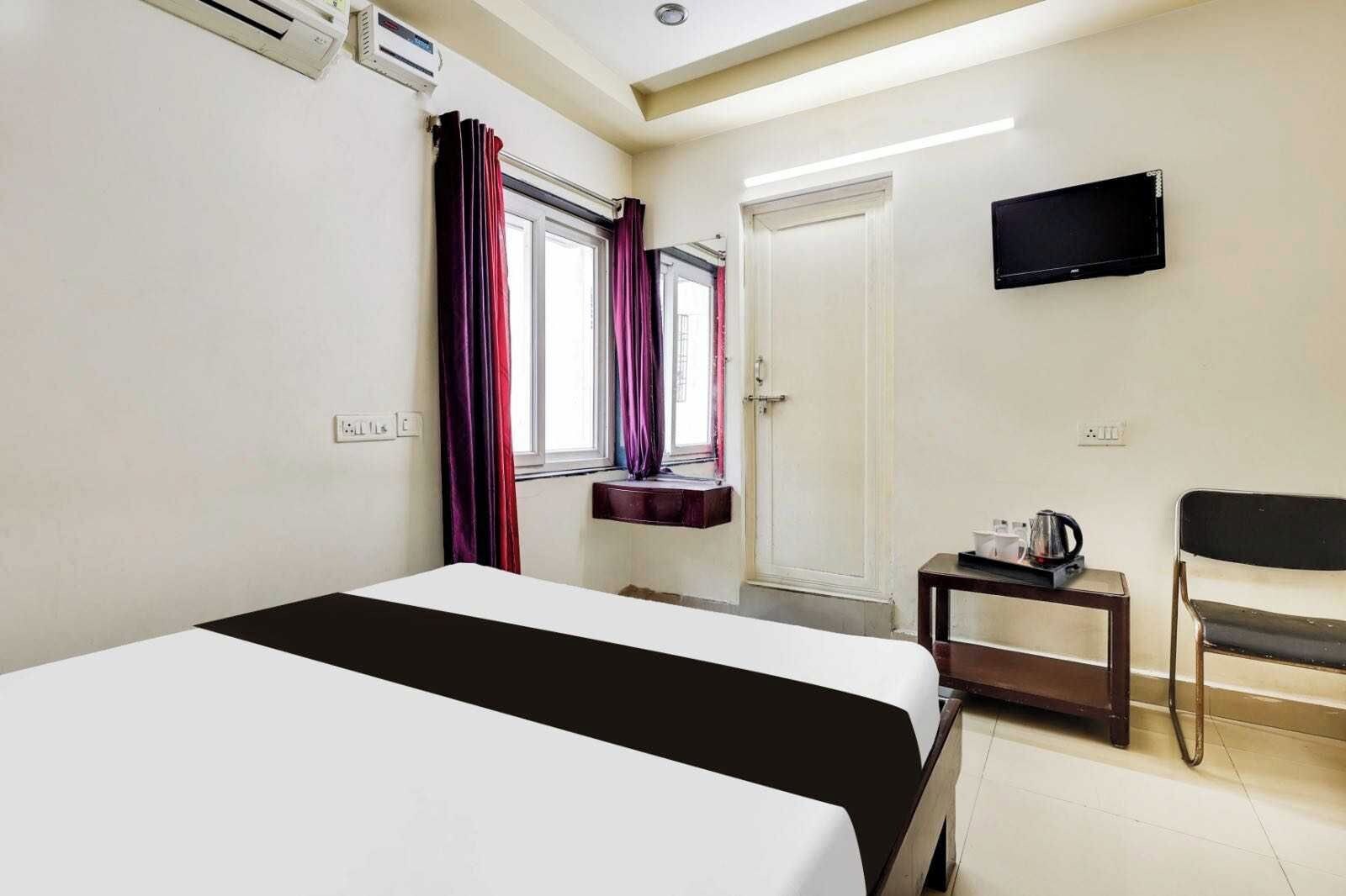 Ein Hotelzimmer mit Bett, Wandfernseher, kleinem Tisch mit Wasserkocher und Stuhl.