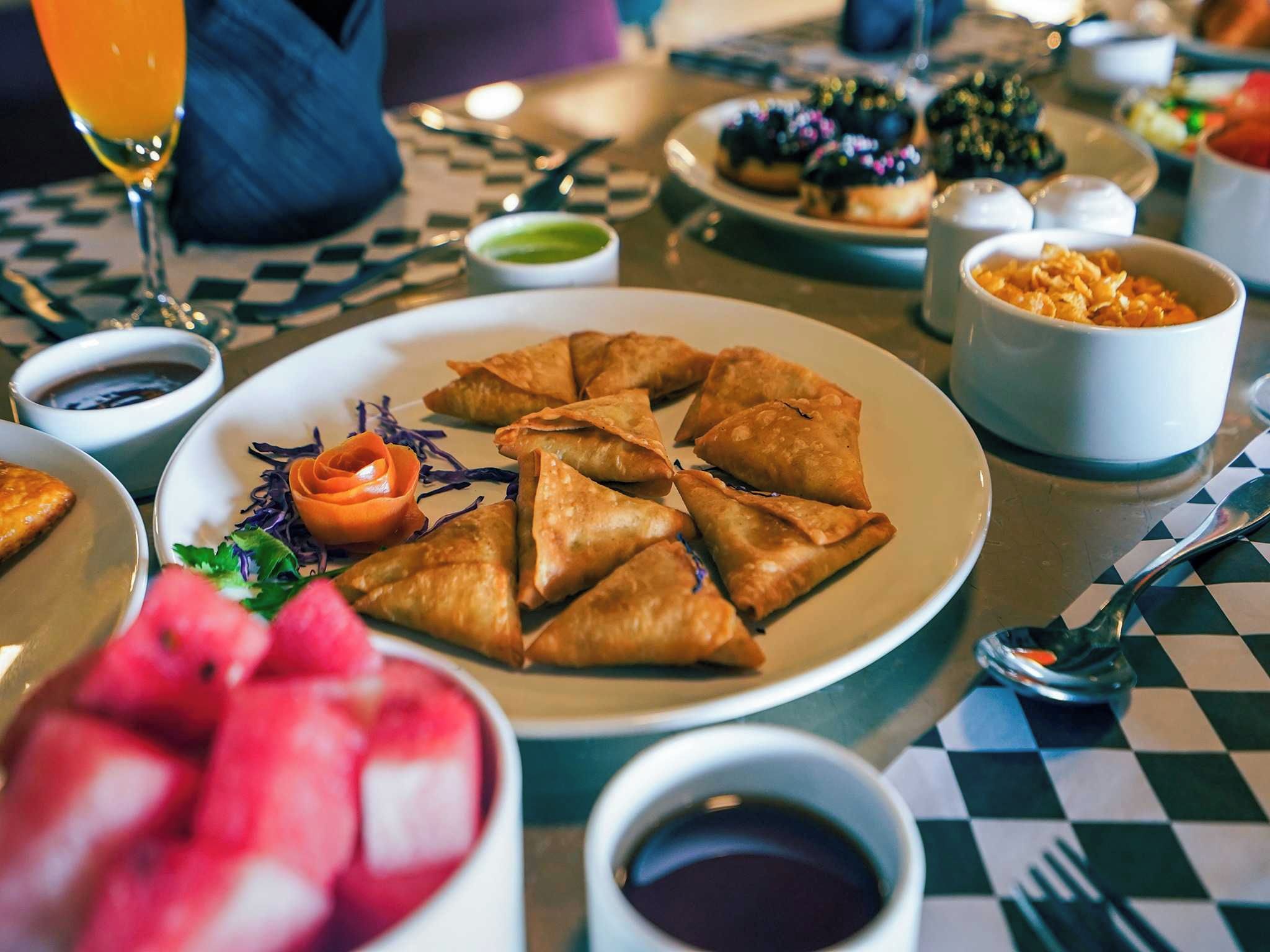 Ein Esstisch mit einer Platte Samosas, einer Schüssel Suppe und einem Glas Orangensaft.