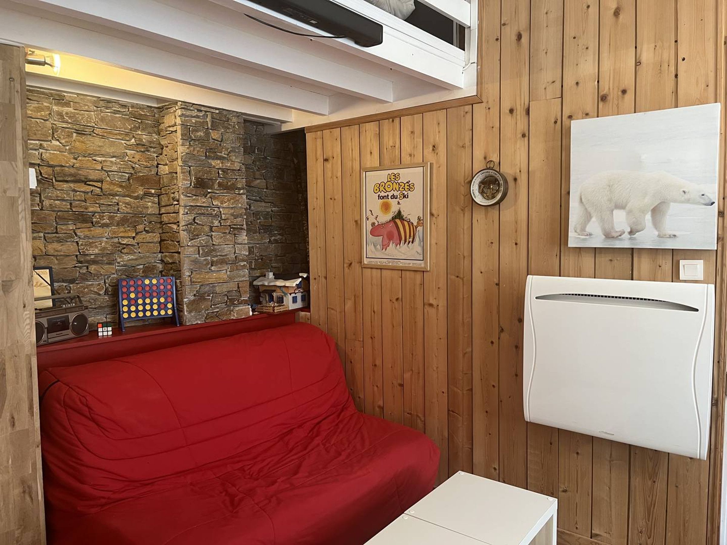 A room with a stone wall, a red sofa, a white table, a framed picture, and a wall-mounted air conditioner.